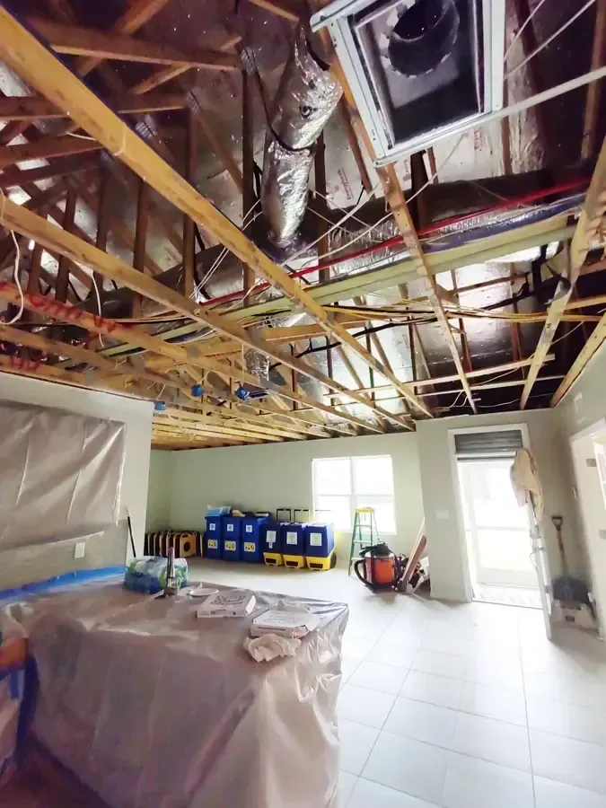 An opened ceiling exposes framing above protected furniture and drying equipment