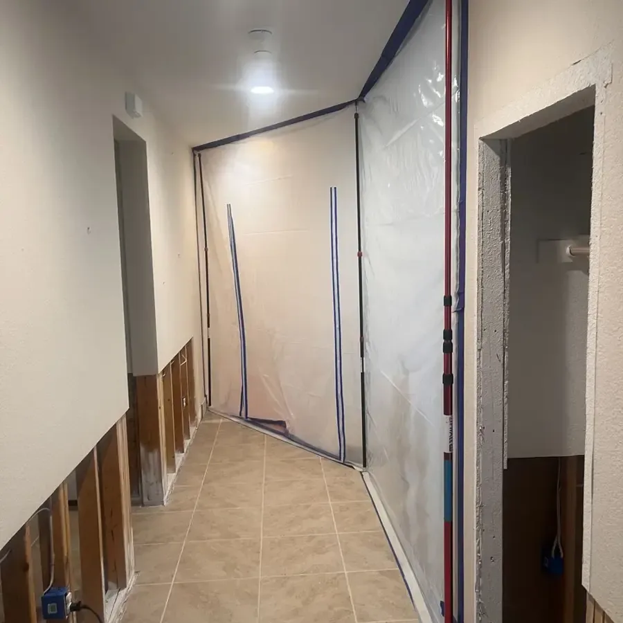 Hallway in a home with containment plastic and drywall cut back for drying