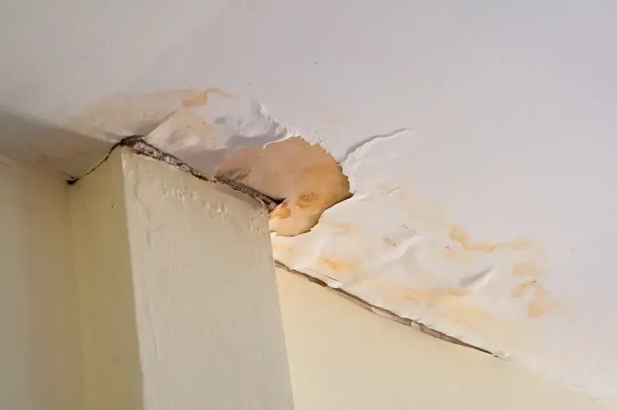 Peeling paint and water stains mark a ceiling above an interior partition
