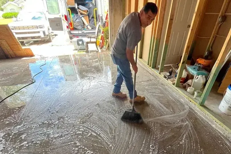 A worker sweeps water across a wet concrete floor toward an open doorway